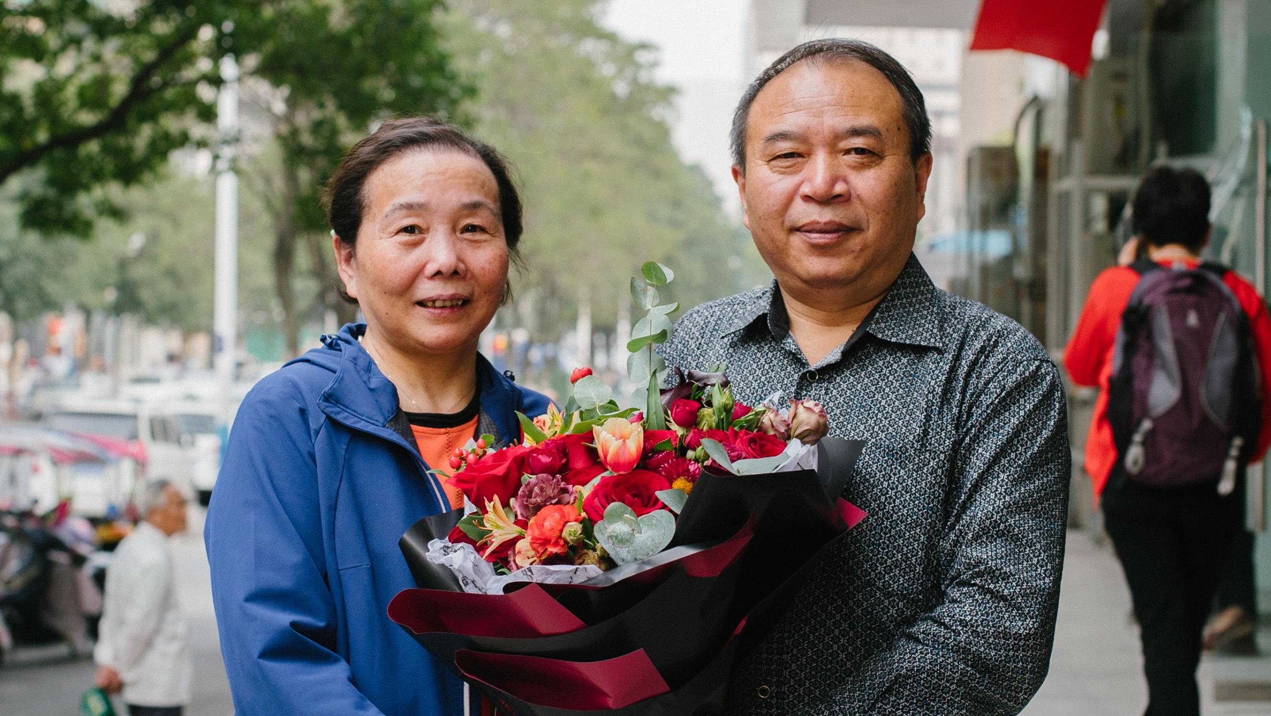 A man and woman stand outside with a bouquet of flowers